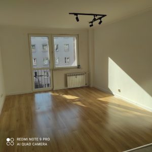 duzy jasny pokoj, z wyjsciem na balkon, drewniane panele, nowoczesny grzejnik, czarna stylowa lampa